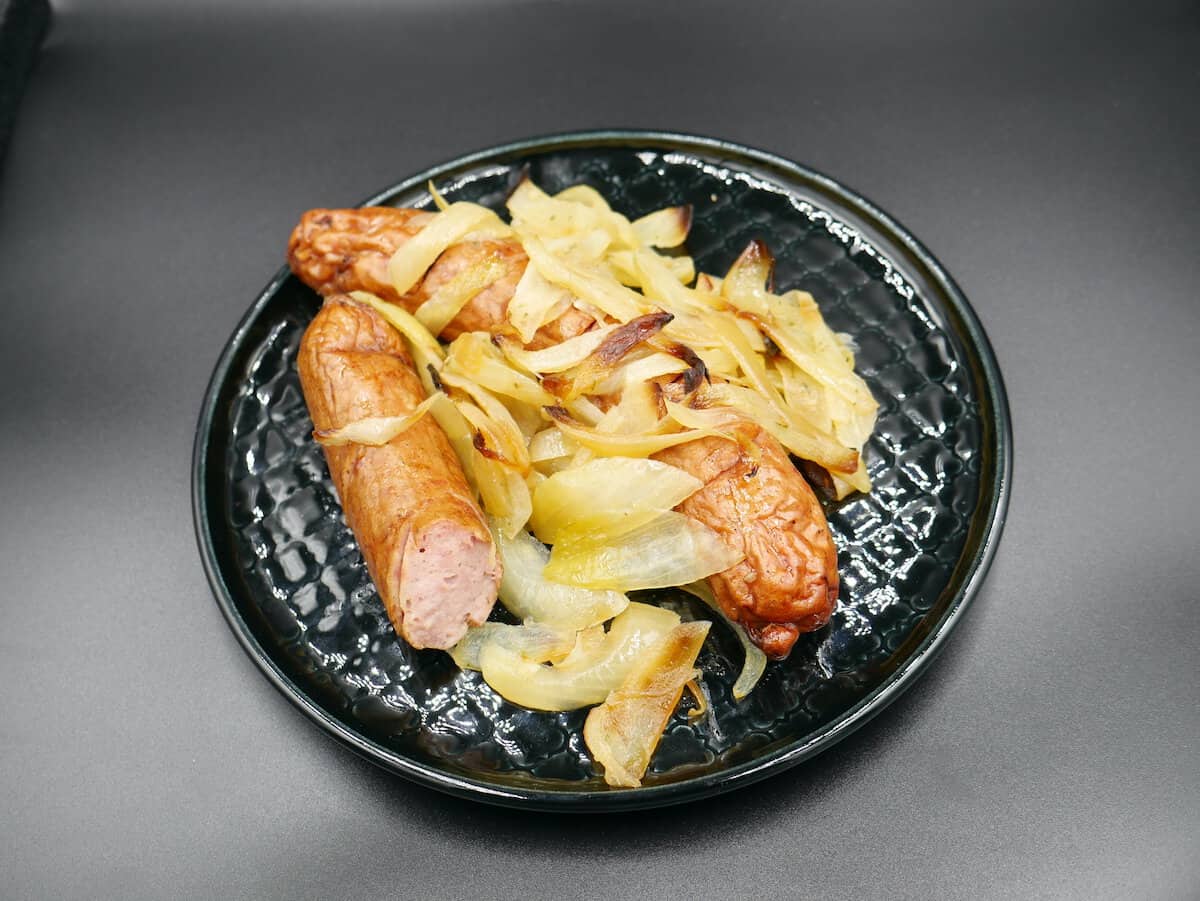 Grilled Polish sausages and saut&eacute;ed onions served on a black plate.
