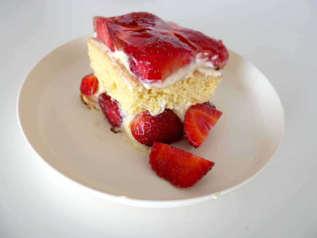 A slice of strawberry shortcake with layers of sponge cake, cream, and fresh strawberries, served on a white plate.