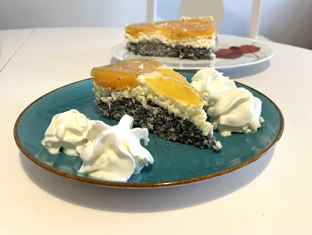 A Polish peach poppy seed cake slice on a plate with whipped cream.