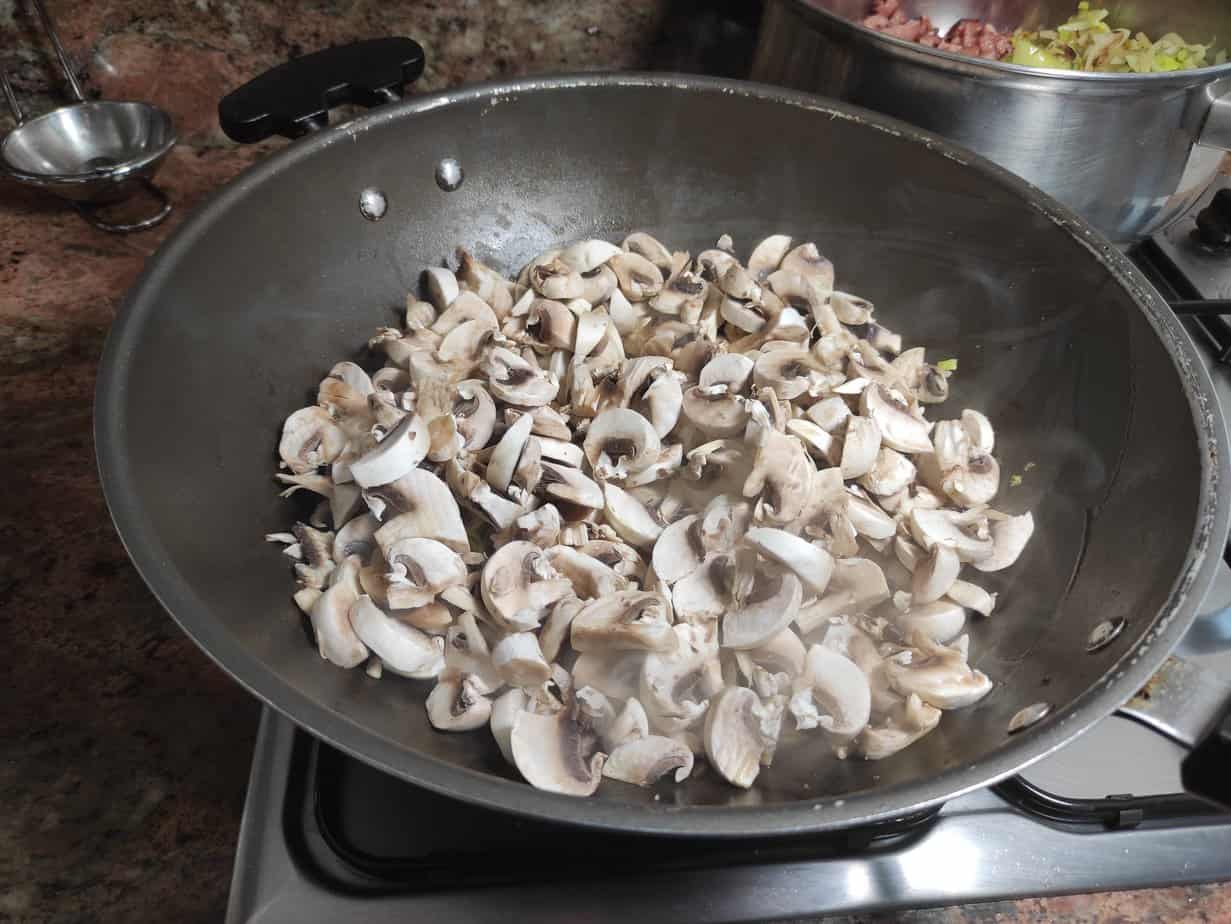 Delicious sliced mushrooms being saut&eacute;ed in a pan on a stove top.
