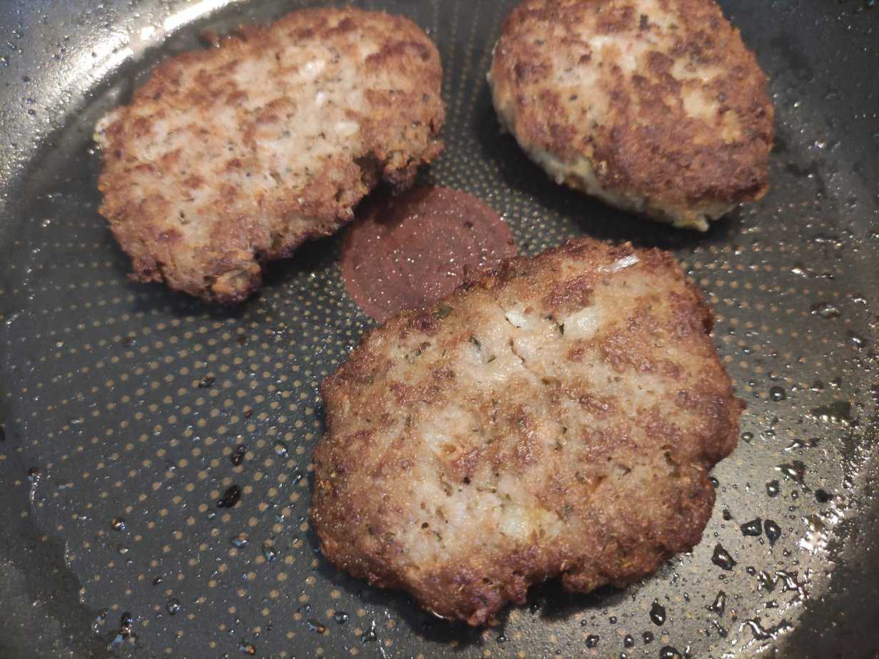 Three cooked hamburger patties in a frying pan, showing a browned and crispy texture, reminiscent of the Famous Steak from the PRL Era.