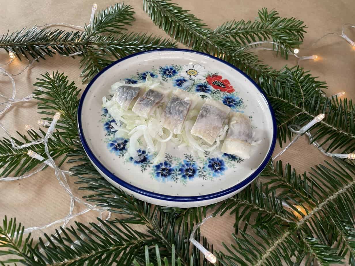 A plate of Polish Herring on a table next to a Christmas tree.
