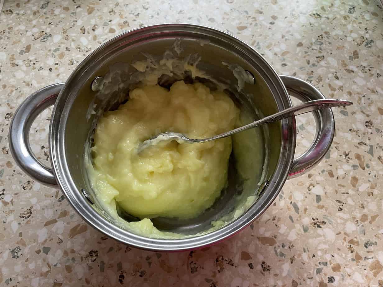 A pot with a spoon in it filled with a caramel cream.