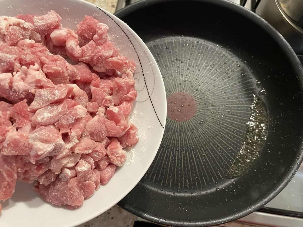 Forszmak Lubelski, a traditional Polish meat stew recipe, showcases raw meat sizzling in a frying pan on a stove.