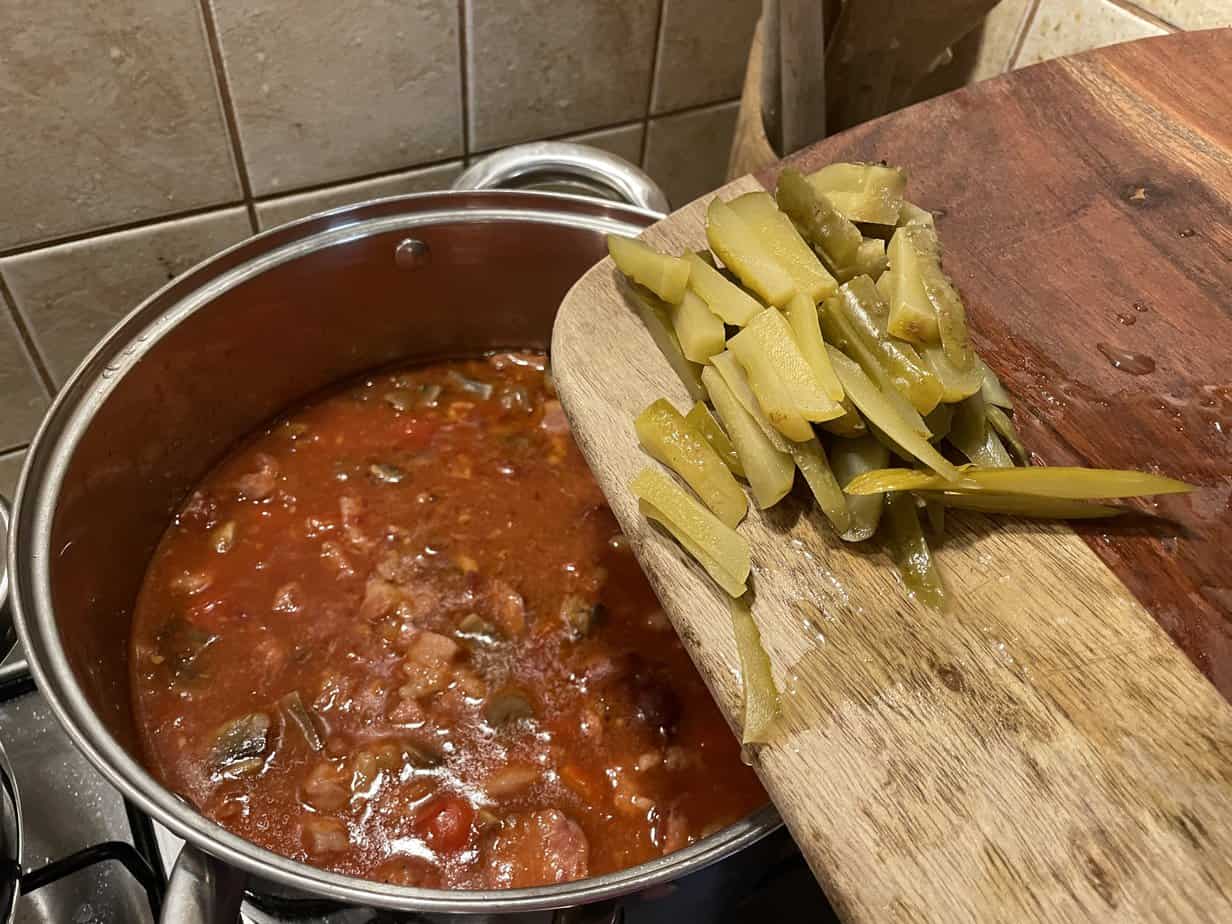A Polish meat stew recipe simmering in a pot on a stove, next to a wooden cutting board.