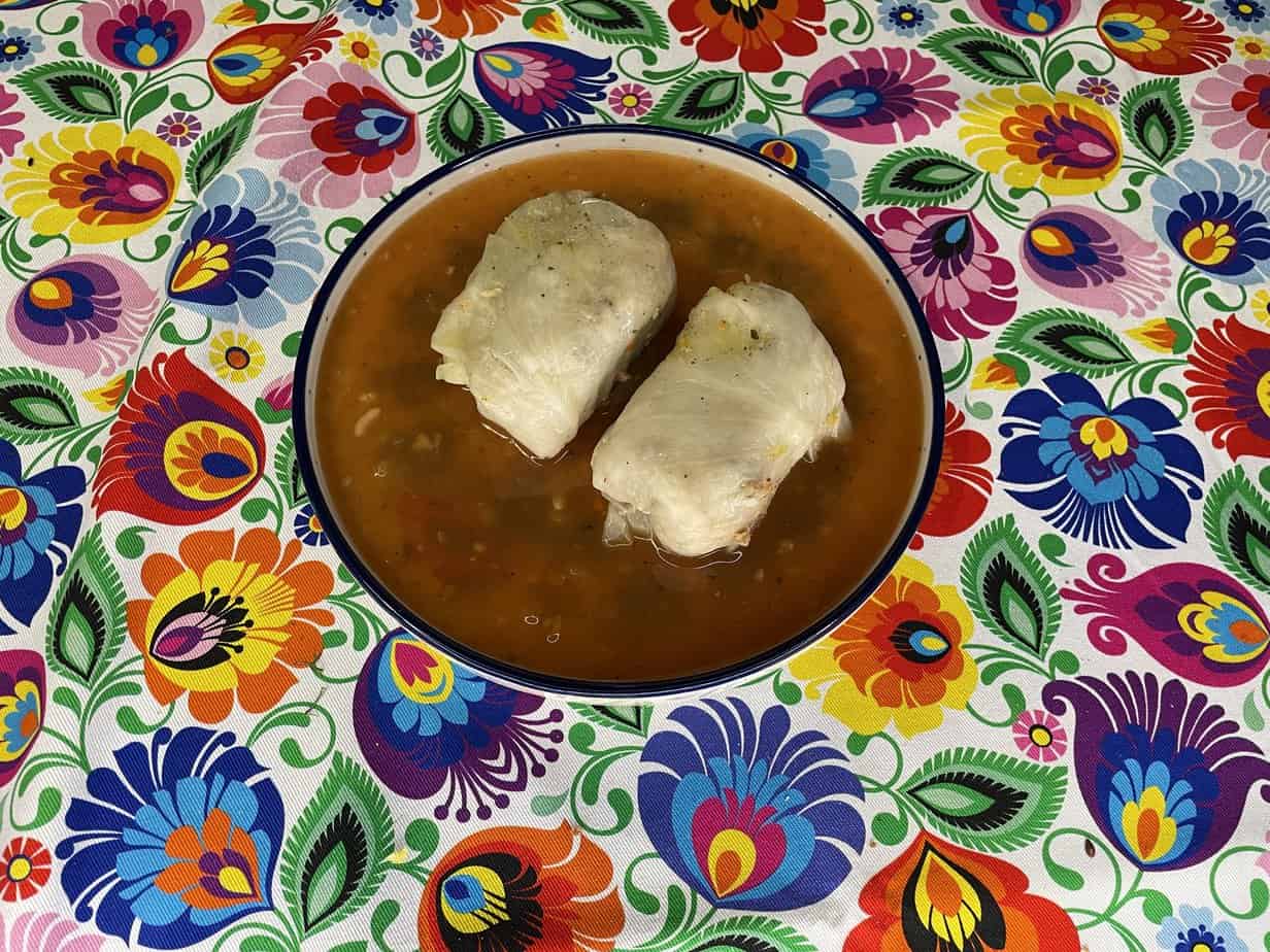 Two tamales in a bowl of broth on a brightly colored floral tablecloth, perfect for celebrating Mother's Day.