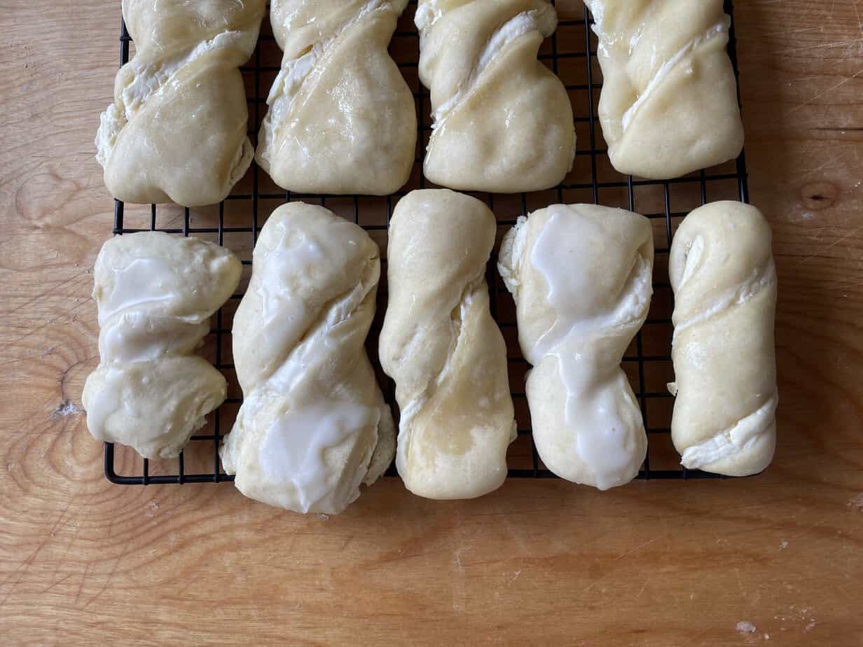 Homemade twisted dough pastries, including some with a white glaze, cooling on a black wire rack placed on a wooden surface. These delightful Zawijane Drożdż&oacute;wki are perfect for any occasion.