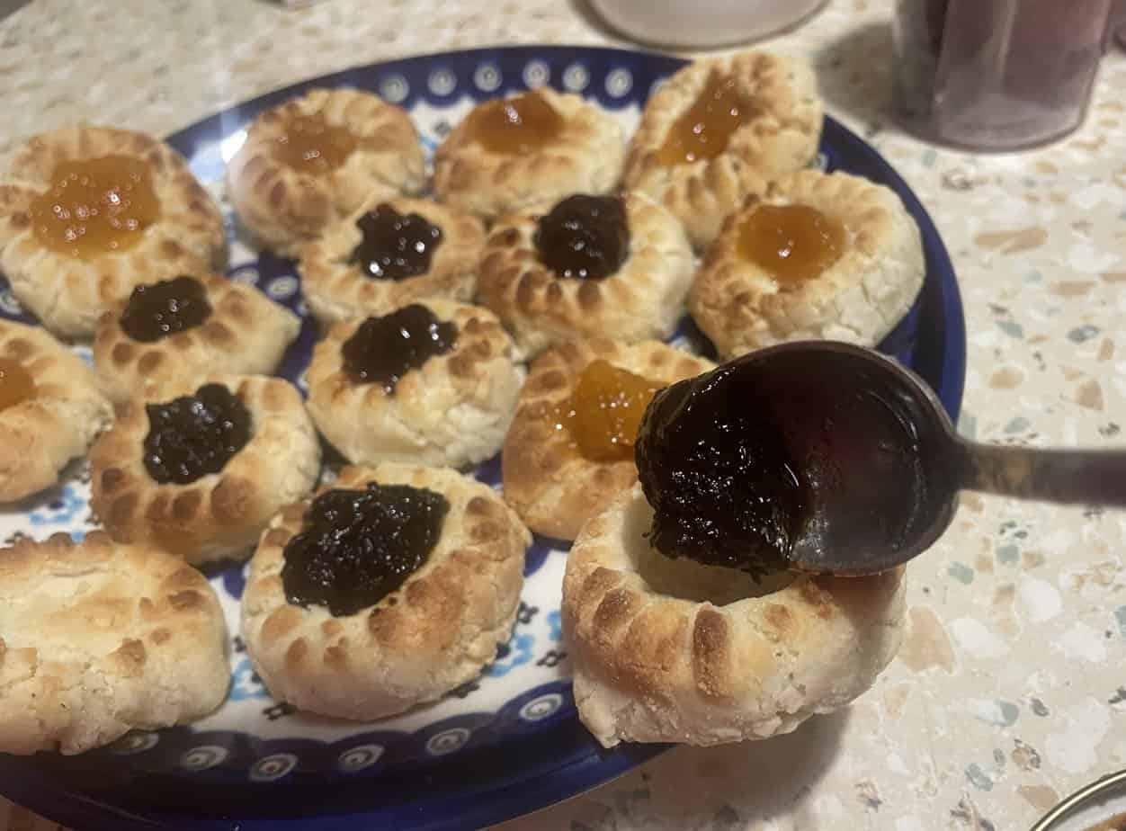 A spoon adding jam to thumbprint cookies on a blue and white patterned plate, reminiscent of traditional Polish Marzipan Cookies, adds an artistic touch.