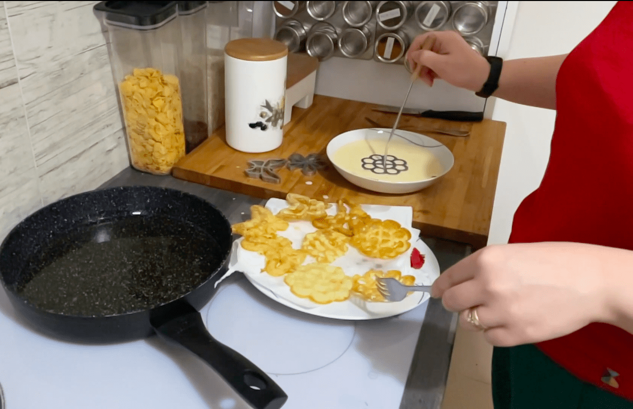 A woman is preparing Polish fried rosette cookies in a kitchen.