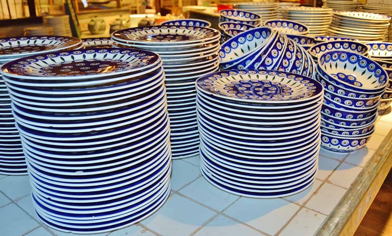 Stacks of ceramic plates with blue and white patterns, inspired by traditional designs from Poland, are arranged on a tiled countertop.
