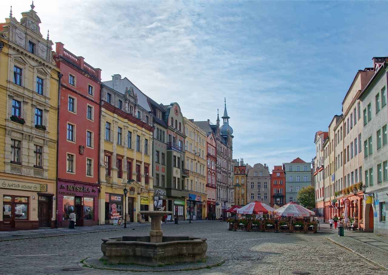 A cobblestone town square in Dolnośląskie, Poland, with colorful historic buildings, a central stone fountain, and outdoor caf&eacute; seating under umbrellas&mdash;one of the charming places to visit in the region.