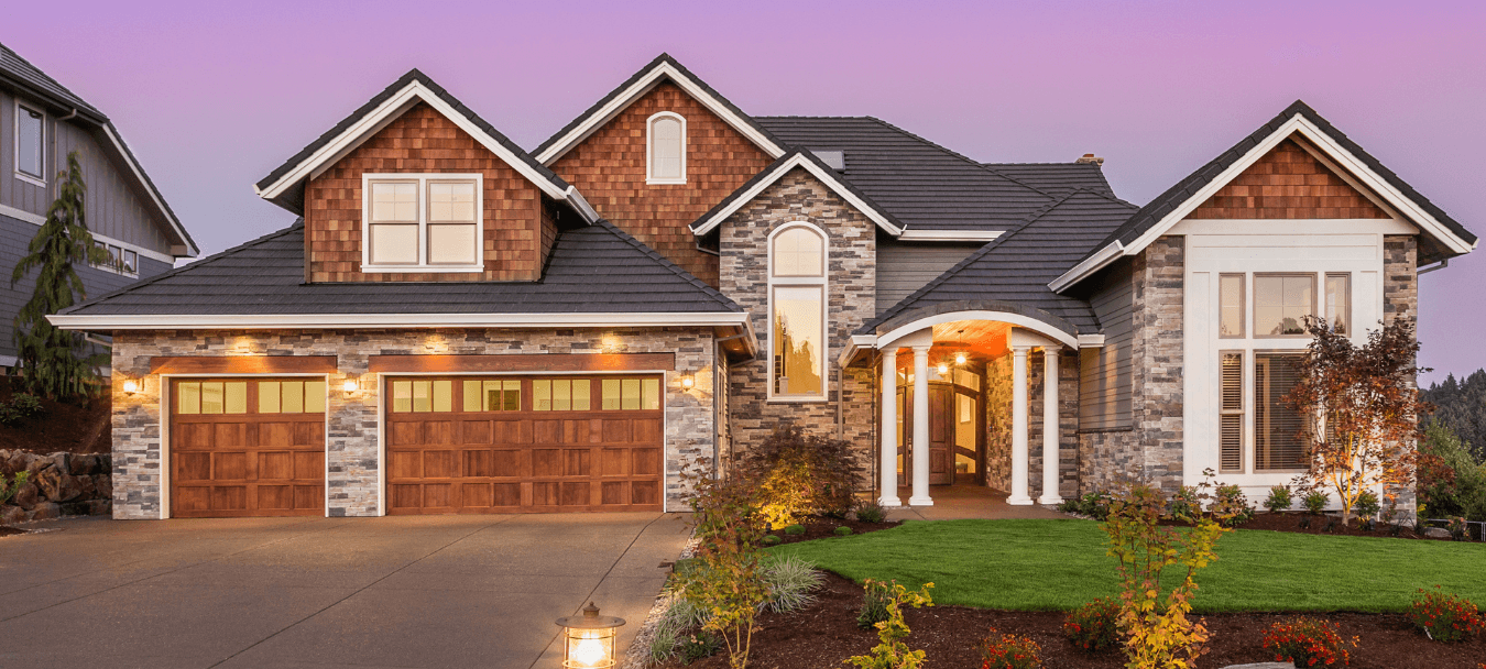 Stunning suburban home with a stone and wood exterior, triple garage, and manicured landscaping at dusk."