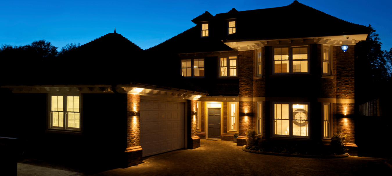 Nighttime exterior of a large, two-story brick home with warm interior lights, highlighting the front garage and main entrance