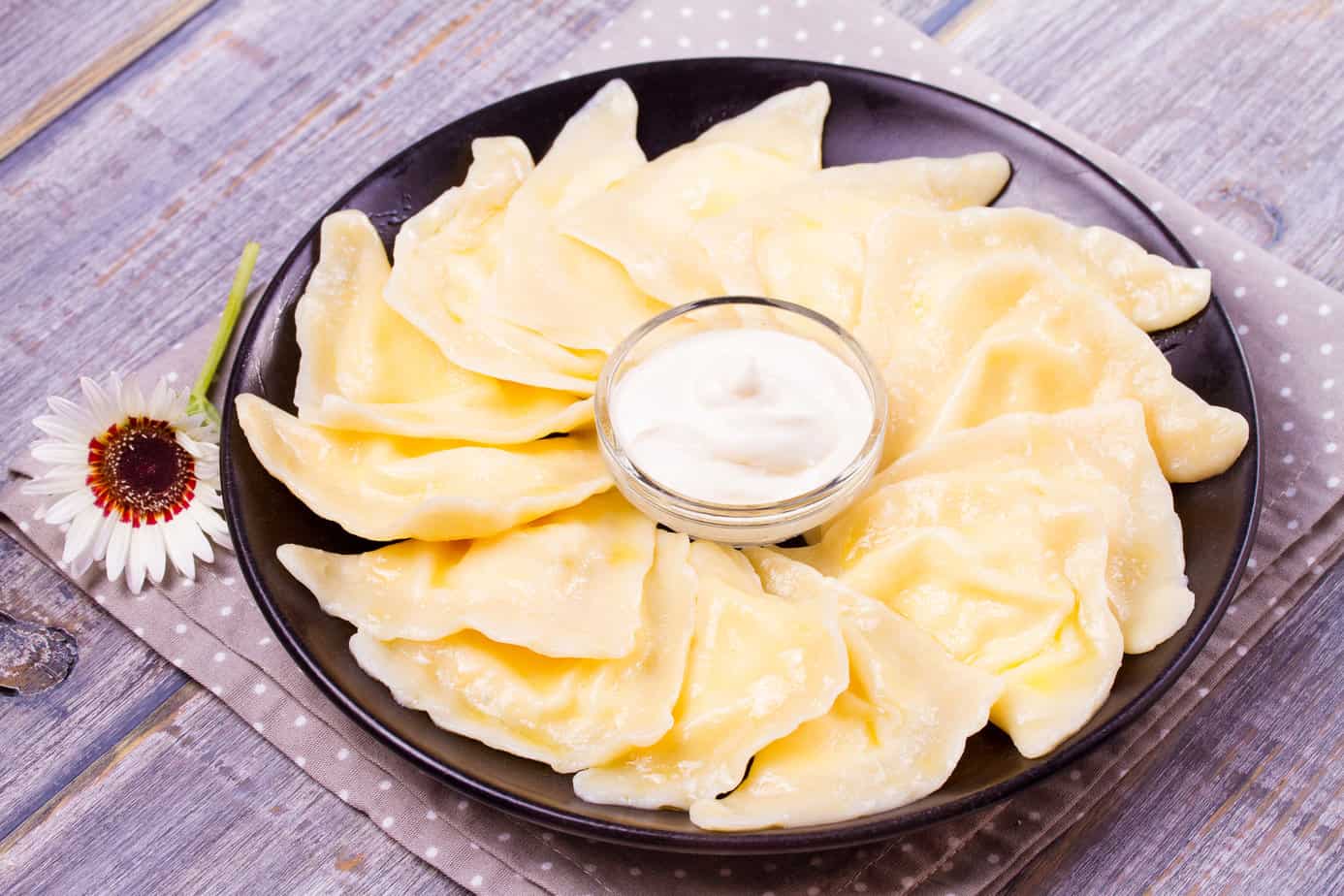A plate of dumplings served with a side of sour cream, the best sauce for pierogi, and garnished with a flower.