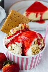 Homemade Strawberry Cheesecake Ice Cream Recipe image 2 strawberry cheesecake ice cream in tub with graham cracker sticking out and strawberry sauce frosted fusions