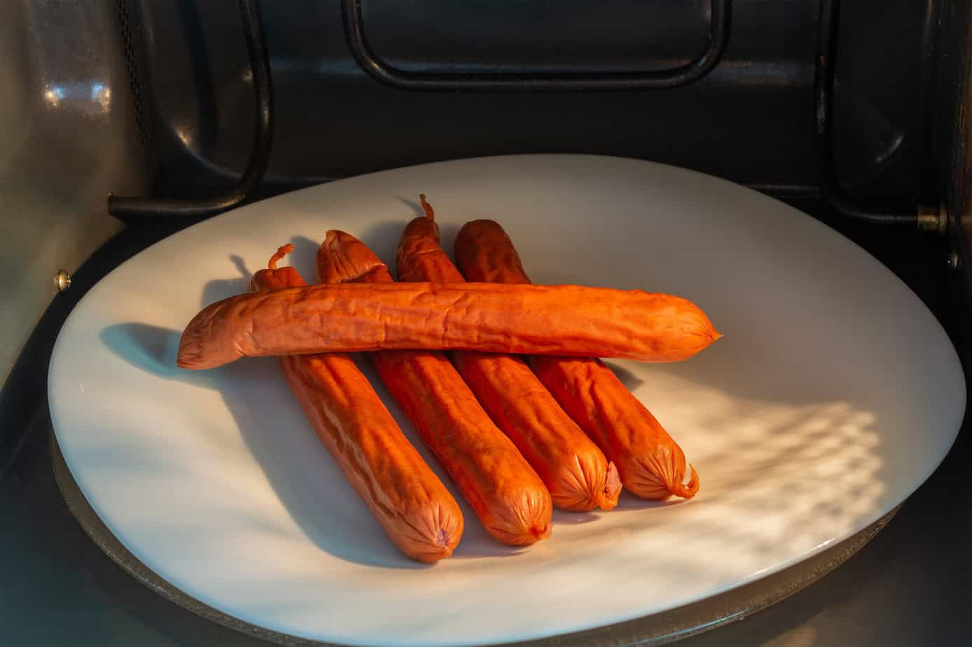 A plate of cooked Polish sausage inside an oven, illuminated by sunlight filtering through a vent.