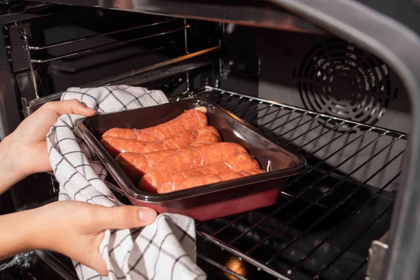 A person places a dish of Polish sausages into an oven to cook.