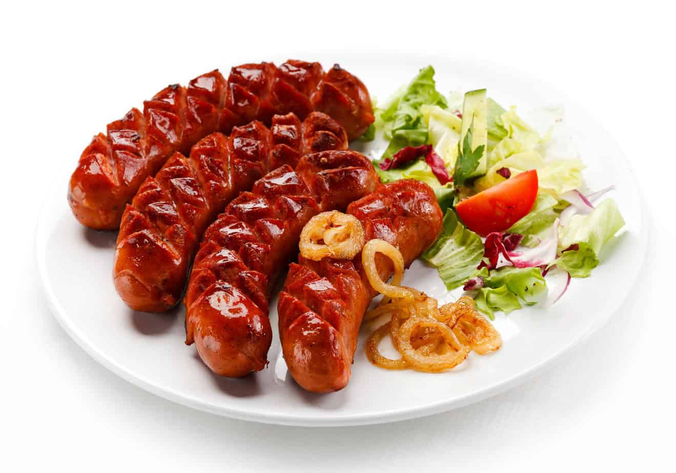 Grilled Polish sausages on a plate with a side salad of lettuce, tomato, and caramelized onions, isolated on a white background.