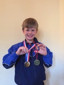 One of the advanced swimmers at Blue Wave Swim School showing his medals after winning swimming competitions for his school