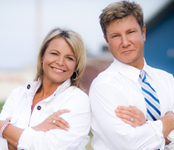 Shannon Barnum and Jim Christl of Modern Market REALTORS® standing side by side with arms crossed, smiling confidently at the camera.