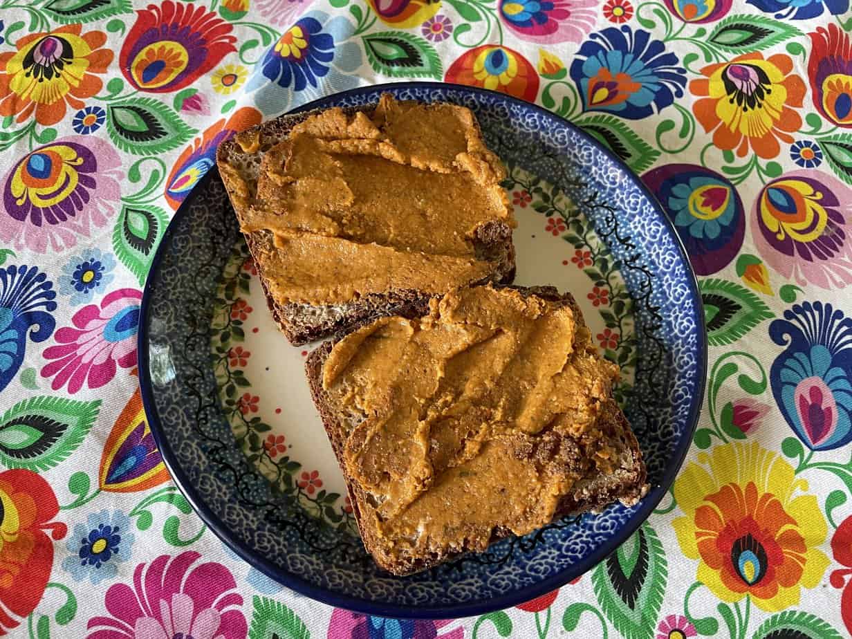 A blue and white plate with two slices of bread spread with almond butter, accompanied by leftover ros&oacute;ł veggies, placed on a colorful floral tablecloth.