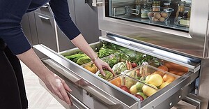 Woman checks produce in refrigerator crisper drawers