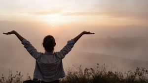 Femme face au lever du soleil qui lève les bras