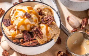 easy-homemade-brown-butter-pecan-ice-cream-image-5-white-bowl-of-brown-butter-and-pecan-ice-crea-with-fresh-pecans-scattered-and-caramel-sauce-drizzled-frosted-fusions