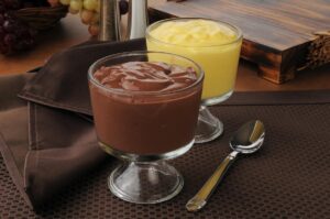 Two bowls of Polish puddings, one chocolate and one vanilla, with a spoon on the side.