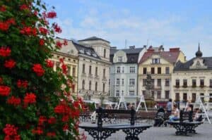 Town square with benches, people sitting, and historic buildings in the background; red flowers in the foreground on the left&mdash;one of the best places to visit when you travel through Slaskie, Poland.