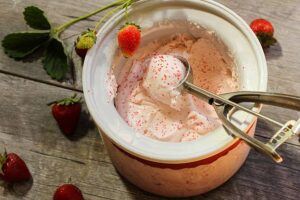 Learn-To-Make-Homemade-Ice-Cream-A-Beginners-Guide-image-12-strawberry-ice-cream-in-churning-bowl-with-ice-cream-scoop-and-fresh-strawberries-scattered-around-frosted-fusions