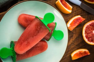 Learn-How-To-Make-The-Perfect-Blood-Orange-Sorbet-image-2-blood-orange-lollies-on-plate-with-pieces-of-blood-orange-inthe-background-Frosted-Fusions-300x200