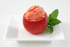 Learn-How-To-Make-The-Perfect-Blood-Orange-Sorbet-image-3-blood-orange-sorbet-served-in-blood-orange-shell-with-fresh-sprig-of-mint-leaves-on-white-square-plate-Frosted-Fusions