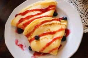 Polish crepes with berries and syrup on a white plate.