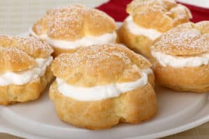 A plate with a group of Polish pastries, known as cream puffs or ptysie, topped with whipped cream and powdered sugar.