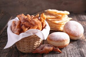 A selection of Polish fried pastries, including doughnuts and crispy thin wafers, served in a basket and on a wooden table for Fat Tuesday.