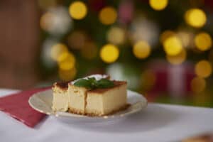 A slice of Polish cheesecake sernik garnished with mint on a plate with festive bokeh lights in the background.