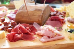 A charcuterie board with various sliced meats including Polish ham, cheeses, and garnishes displayed on a wooden surface.