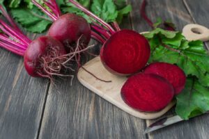 Whole and sliced beets from the best Polish recipes on a wooden cutting board with attached fresh leaves on a dark wooden surface.
