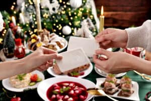 Two people exchange Opłatek over a festive table adorned with dishes, candles, and a decorated tree in the background, embracing the warmth of Polish Christmas traditions.
