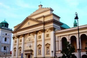 A neoclassical church building with ornate columns and statues on the facade, under a clear blue sky.