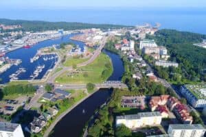 Aerial view of a coastal city in Zachodniopomorskie, Poland, with a river, marina, green spaces, residential buildings, and industrial areas near the shoreline&mdash;one of the best places to visit.
