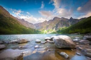 Large rocks line the foreground of Morskie Oko, a clear mountain lake near Zakopane, with green slopes and rugged peaks rising under a partly cloudy sky&mdash;a must-see spot for travel tips in the Tatra Mountains.