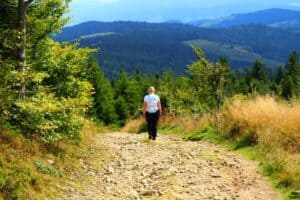 A person with a backpack walks alone on a rocky trail through a forested mountain landscape under a clear sky, capturing the spirit of solo travel Poland for those seeking adventure and inspiration.