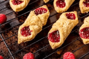 Freshly baked raspberry Kolacky pastries cooling on a wire rack.
