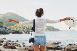 Femme debout chapeau à la main face à la mer