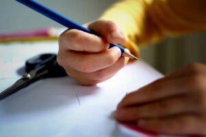 enfant qui écrit sur un cahier avec un crayon en bois