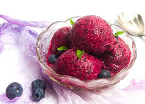 A Refreshing and Healthful Homemade Blueberry Sorbet image 1 scoops of blueberry sorbet in glass dish with fresh blueberries scattered around frosted fusions