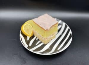 A slice of pink Polish lemon cake on a black and white plate.