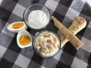 A bowl of yogurt with other ingredients on a checkered tablecloth.